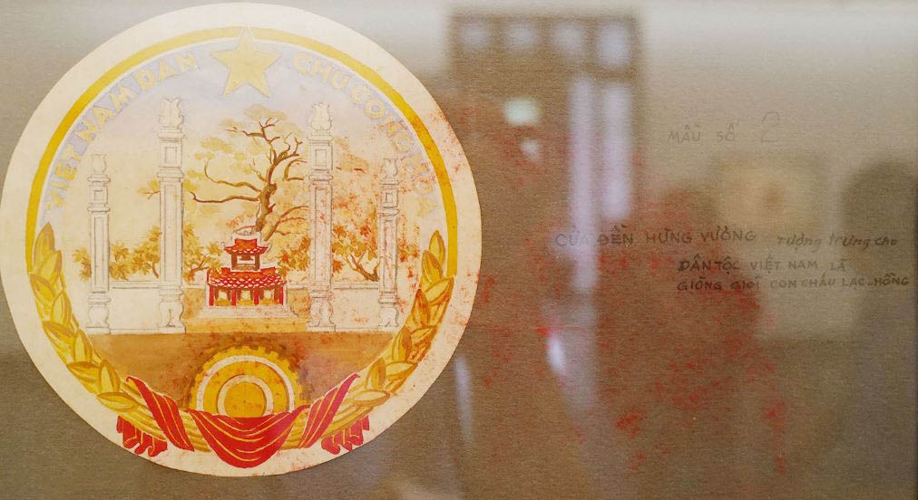 Phác thảo Quốc huy Việt Nam Dân chủ Cộng hòa, bản vẽ màu của họa sĩ Bùi Trang Chước với cây cổ thụ phía sau cửa đền Hùng, dải lụa đỏ uốn quanh những bông lúa chín vàng, bánh xe, ngôi sao vàng 5 cánh. Mẫu Quốc huy này tượng trưng cho dân tộc Việt Nam là dòng dõi con cháu lạc hồng.