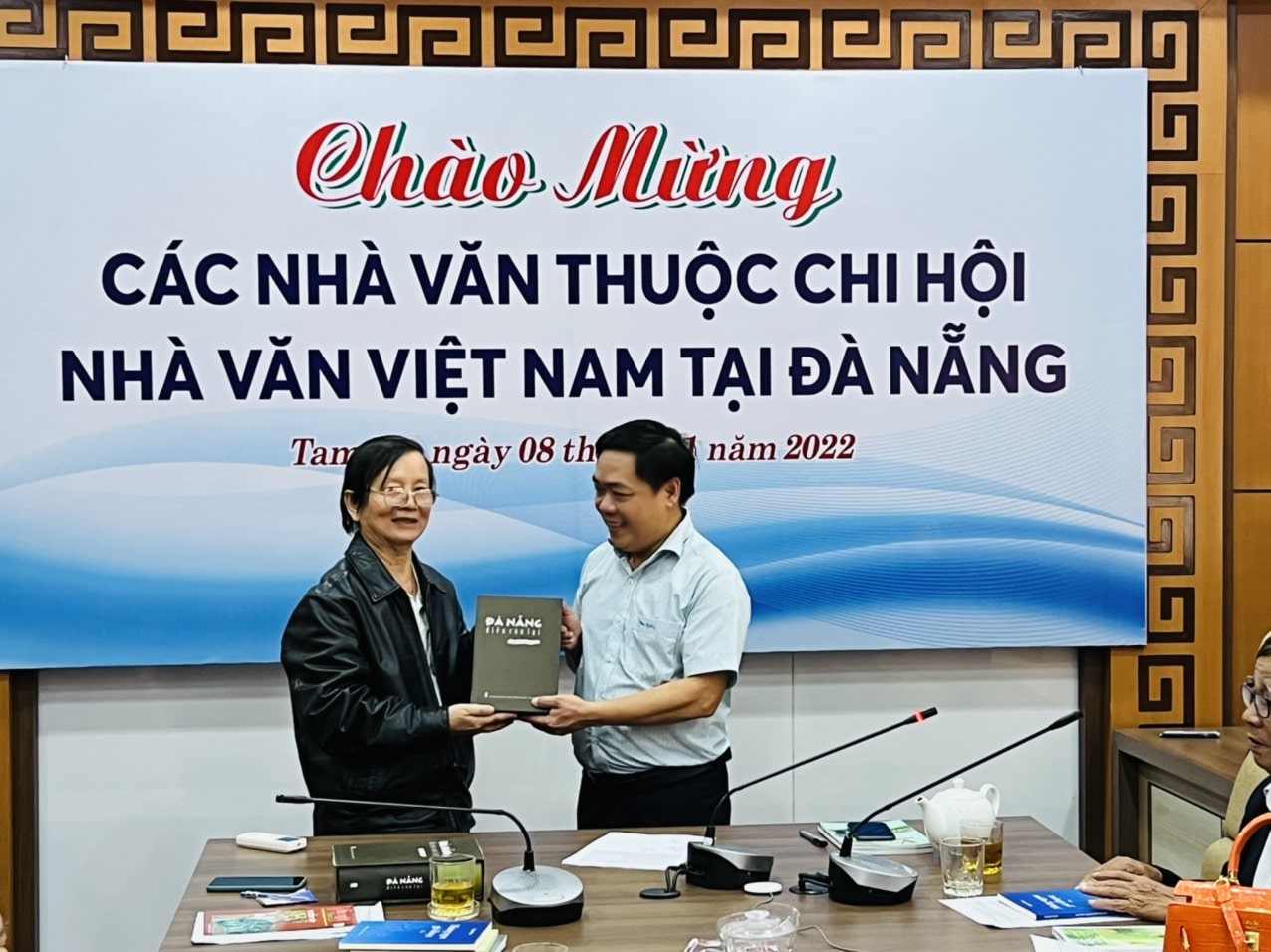 Nhà thơ, Dịch giả Bùi Xuân (bìa trái) tặng tác phẩm "Điều còn lại" (Tuyển tập thơ văn của Nhà văn Việt Nam tại Đà Nắng) cho Chủ tịch UBND Thành phố Tam Kỳ Bùi Đức Ảnh 