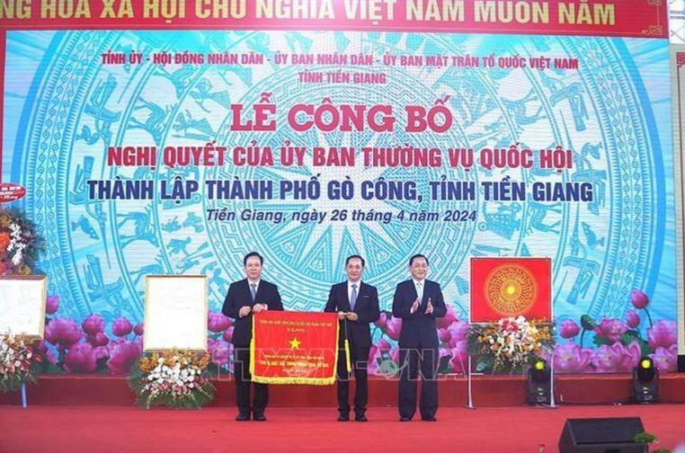 Thừa ủy quyền, đồng chí Nguyễn Văn Vĩnh, Phó Bí thư Tỉnh ủy, Chủ tịch UBND tỉnh Tiền Giang (phải) trao Cờ thi đua cho lãnh đạo thành phố Gò Công.