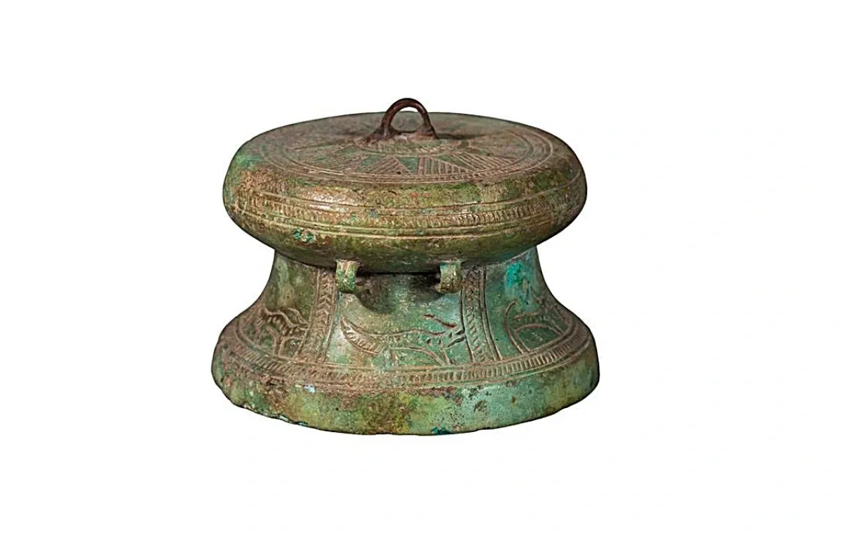 Trống Minh khí, chất liệu đồng, đường kính mặt 7 cm, cao 5 cm. Trống có hình dáng tương tự trống Làng Vạc I, II, III, thuộc dạng trống thấp lưng choãi. Trống có tang phình, thân hình nón cụt, loe dần xuống dưới, chân trống thấp. Trống có 2 đôi quai kép ở hai bên thân. Chính giữa mặt trống cũng gắn một quai tương tự để làm móc treo. Tuy nhiên, trong khi quai ở thân được đúc liền, thì quai trên mặt trống được gắn vào sau khi đúc. (Ảnh: Bảo tàng Nghệ An cung cấp).
